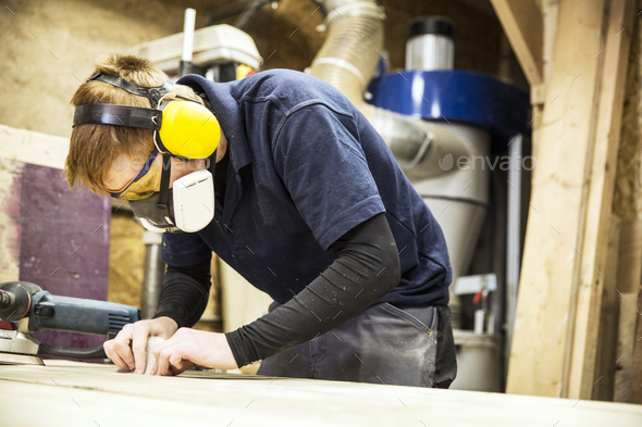 Man wearing ear protectors, protective goggles and dust mask standing in a warehouse, working on a