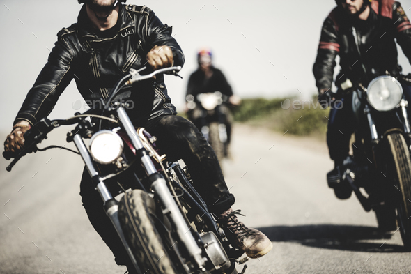 Three men wearing leather jackets riding cafe racer motorcycles along rural  road. Stock Photo by Mint_Images