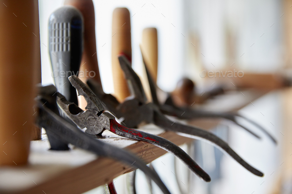 A violin maker\'s workshop. A rack of hand tools along the window.