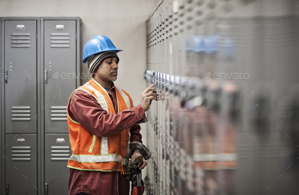 Black man factory worker wearing safety vest and getting into his locker in a factory break room.