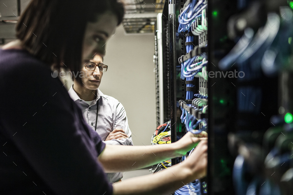 Caucasian woman and man technicians working on CAT 5 cables in a large computer server farm.