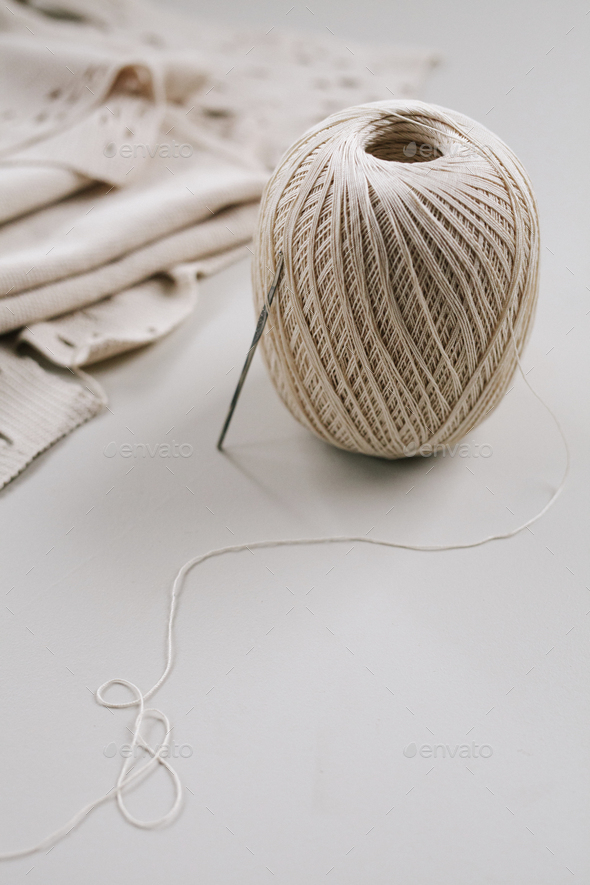 A ball of string or thread and a metal crochet hook or needle with folded fabric.