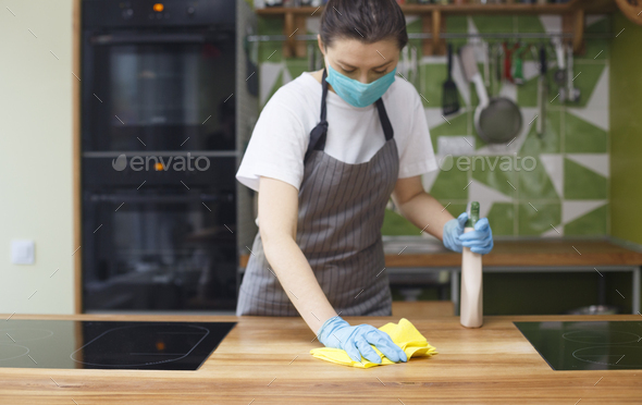 Woman cleaning kitchen with disinfecting spray and microfiber