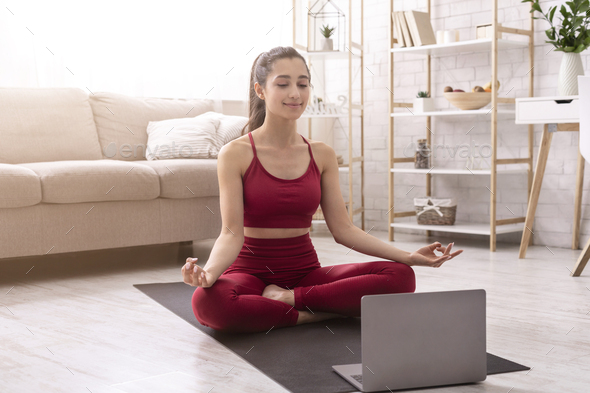 Tranquil girl doing her morning yoga or meditation to online streaming practice at home