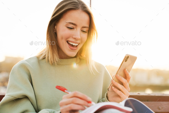 Portrait of woman using cellphone and studying with exercise books