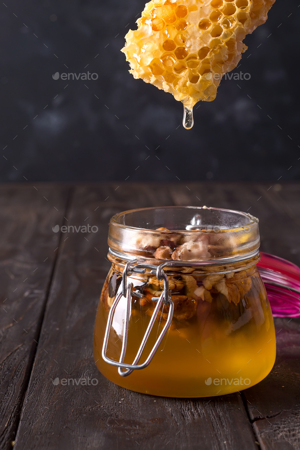 honey comb dripping from dipper into jar with nuts on old wooden table.  Healthy eat Stock Photo by lyulkamazur