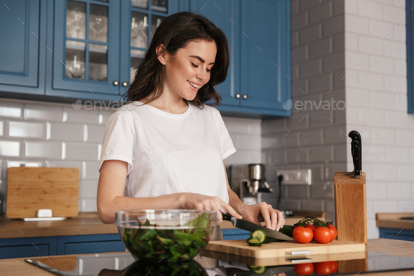 Beautiful young brunette woman cooking salad