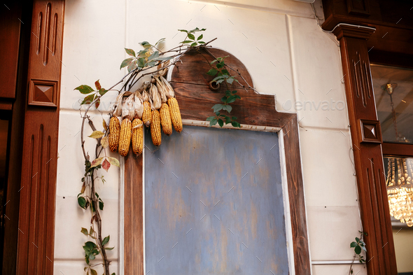 Corn on wooden board with space for text in city street, holiday autumnal decoration of store fronts