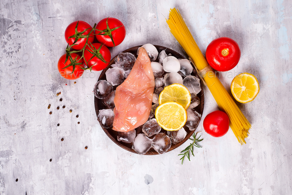 Pasta ingredients. Chicken breasts, tomatoes, spaghetti pasta, and lemon on the stone table - Stock Photo - Images