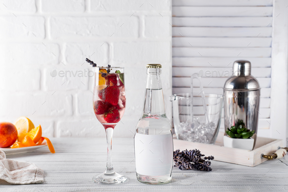 Red Cocktail with ice and strawberry, ginger and lavender with a bottle of tonic and a place under - Stock Photo - Images