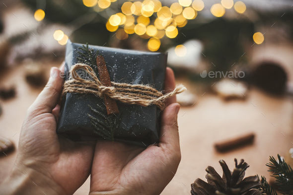 Hands holding rustic christmas gift in black wrapping paper - Stock Photo - Images