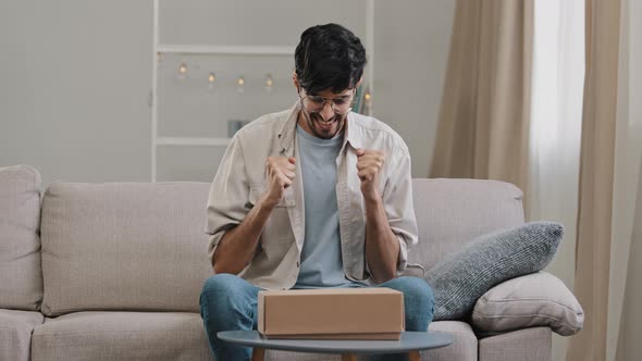 Young Customer Birthday Man Bearded Guy Client with Glasses Sits at Home on Couch with Cardboard Box alt