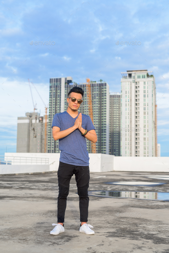 Full body shot of young handsome multi ethnic man with sunglasses against  view of the city