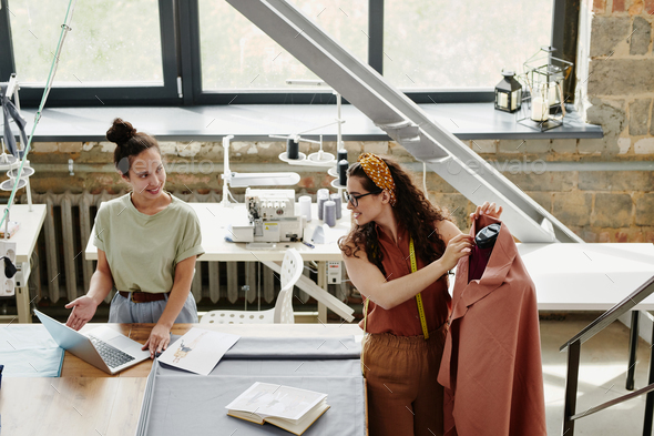 Happy young designer of fashion showing her colleague new models - Stock Photo - Images