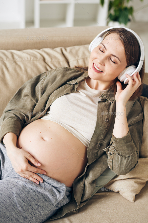 Young serene pregnant woman with headphones listening to calm music and relaxing