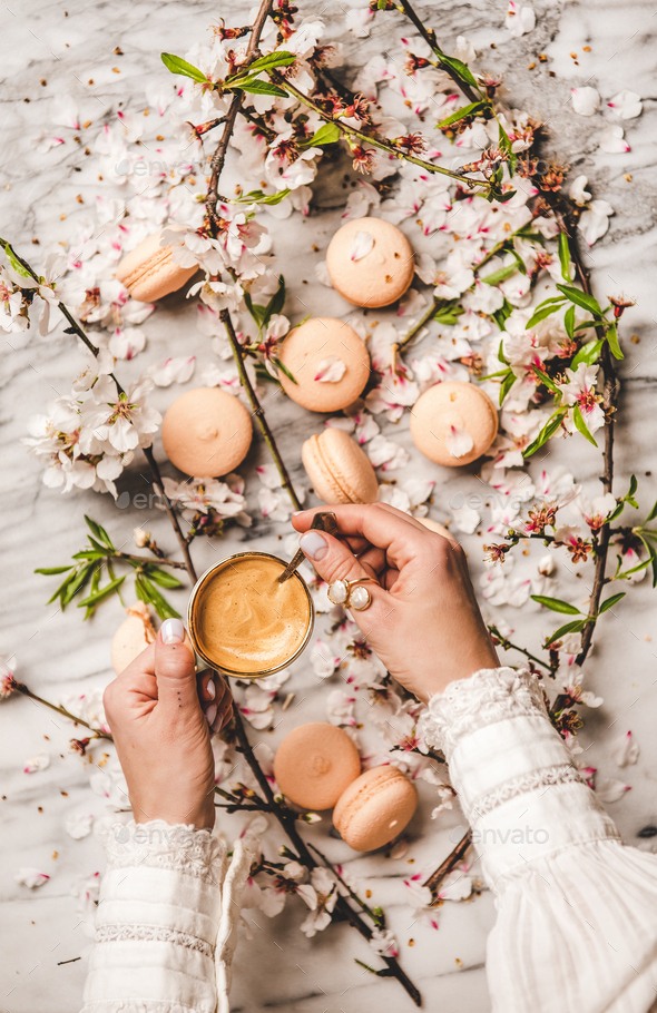 Womans hands holding fresh coffee over macaron cookies and flowers - Stock Photo - Images