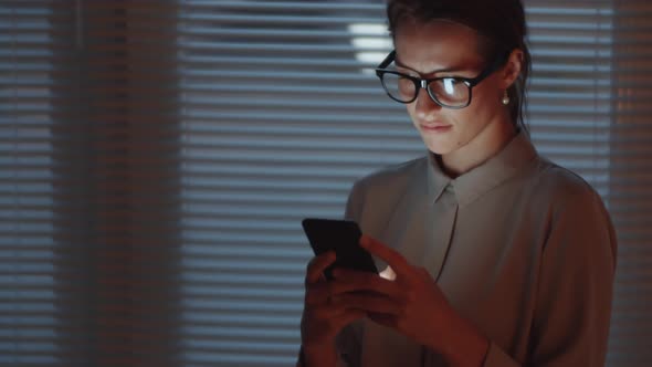 Young Businesswoman Typing on Smartphone in Dark Office alt