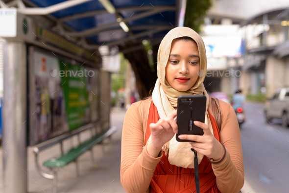 Young beautiful Indian Muslim woman using phone at the bus stop