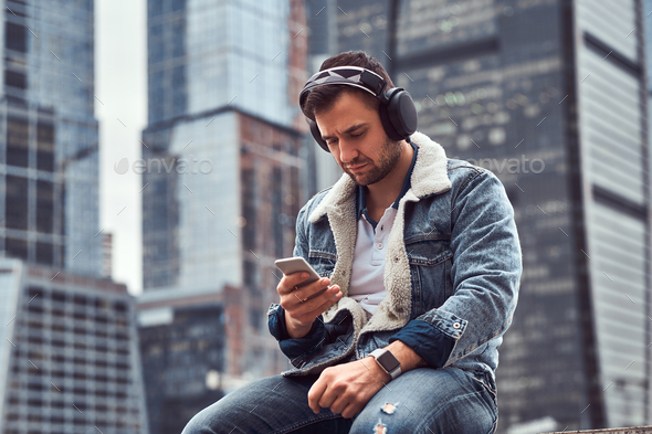 Trendy dressed male sitting in front of skyscrapers in Moscow city at cloudy morning - Stock Photo - Images