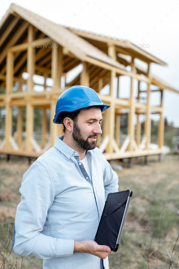 Builder near the wooden house on the construction site - Stock Photo - Images
