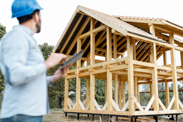 Builder with touchpad near the wooden house on the construction site - Stock Photo - Images