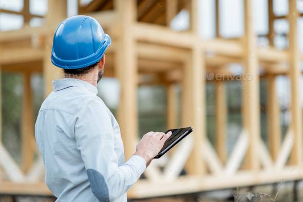 Builder with digital touchpad near the wooden house on the construction site - Stock Photo - Images