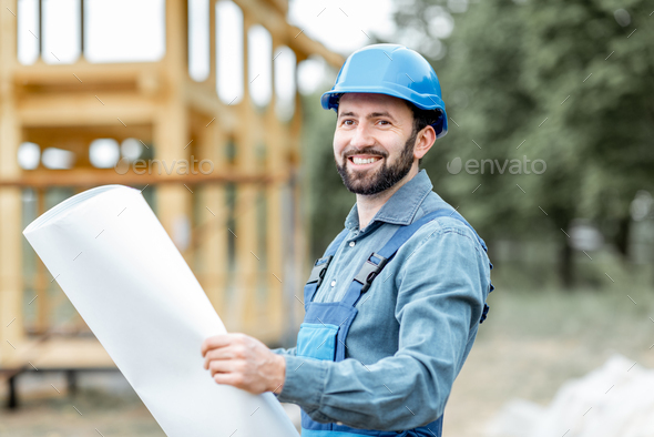 Builder with blueprints near the wooden house on the construction site - Stock Photo - Images