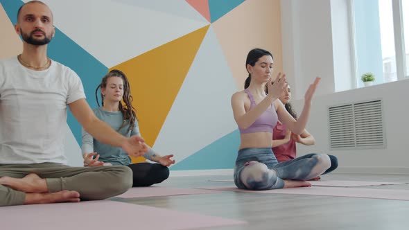 Girls and Guy Enjoying Meditation During Yoga Practice in Cozy Studio Sitting in Lotus Pose alt