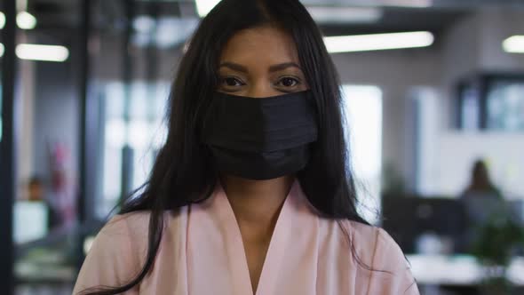 Portrait of mixed race businesswoman wearing face mask standing in office looking to camera alt