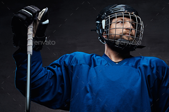 Portrait of a bearded ice-hockey player in a blue sportswear with gaming stick. Studio shot.