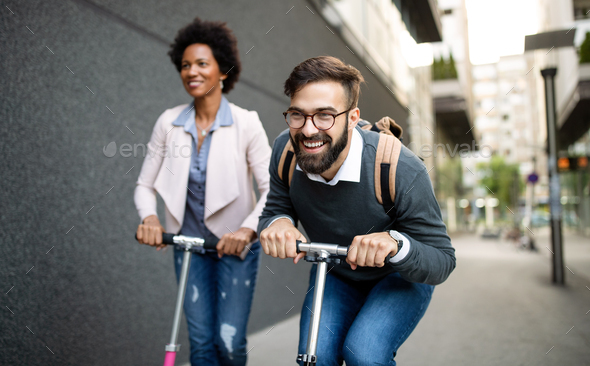 Two smiling business people driving electric scooter going to work