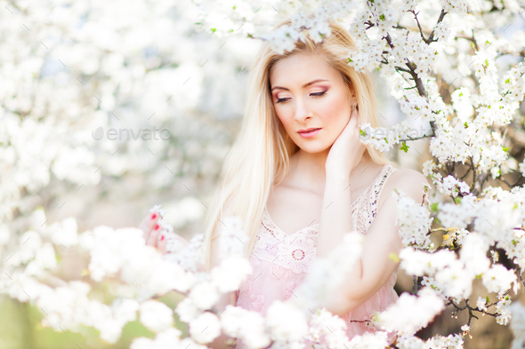 Young beautiful blonde smiling woman in white mini dress standing with blooming trees at background - Stock Photo - Images