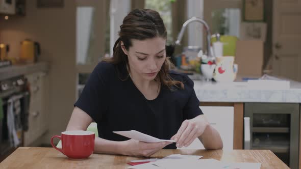 Young adult woman opening bills at home on kitchen table