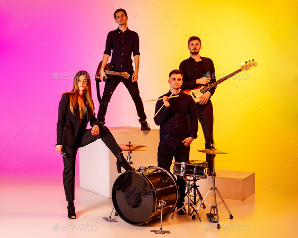Young caucasian musicians, band performing in neon light on gradient studio background - Stock Photo - Images