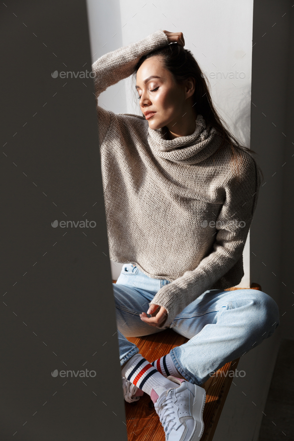 Image of relaxed asian woman sitting on window sill