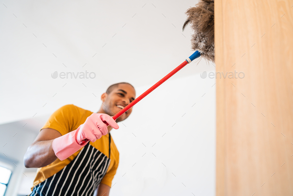 Young latin man dusting his new house.