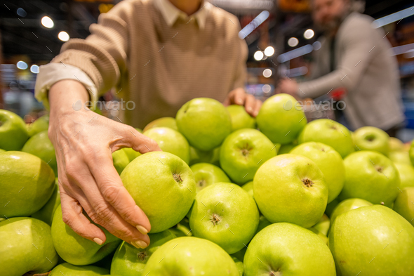 Hand of mature female consumer choosing fresh granny smith apples