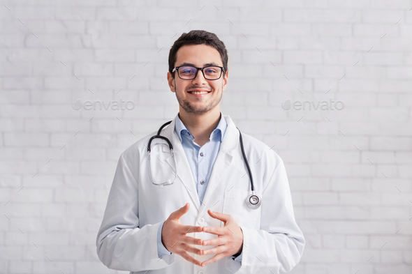 Remote work. Young doctor in white coat on brick wall background