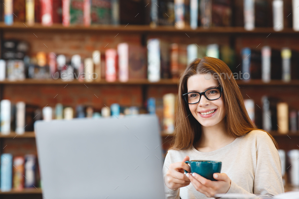 Beautiful young girl with coffee mug working on laptop and smiling