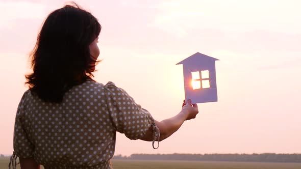 Girl Holding a Paper House. The Concept of Construction, Real Estate Transactions and a Happy Family alt