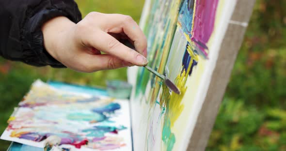 the Artist's Hand with a Brush and a Drawing Tool Working with Canvas Against the Background of alt