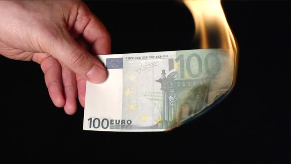 A human hand holds one hundred euro flaming on a black background