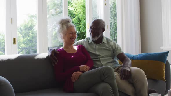 Portrait of mixed race senior couple smiling while sitting on the couch at home alt