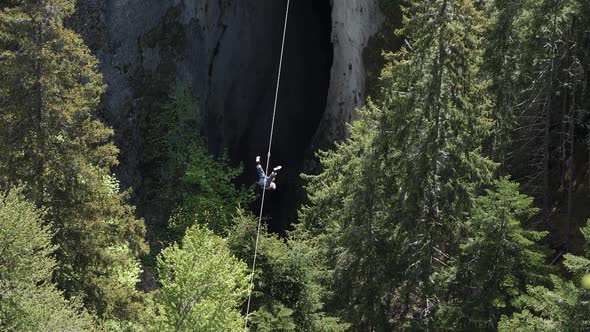 A Young Man Descends Extremely on a Rope with a Reel in the Mountains between Huge Rock Formations alt