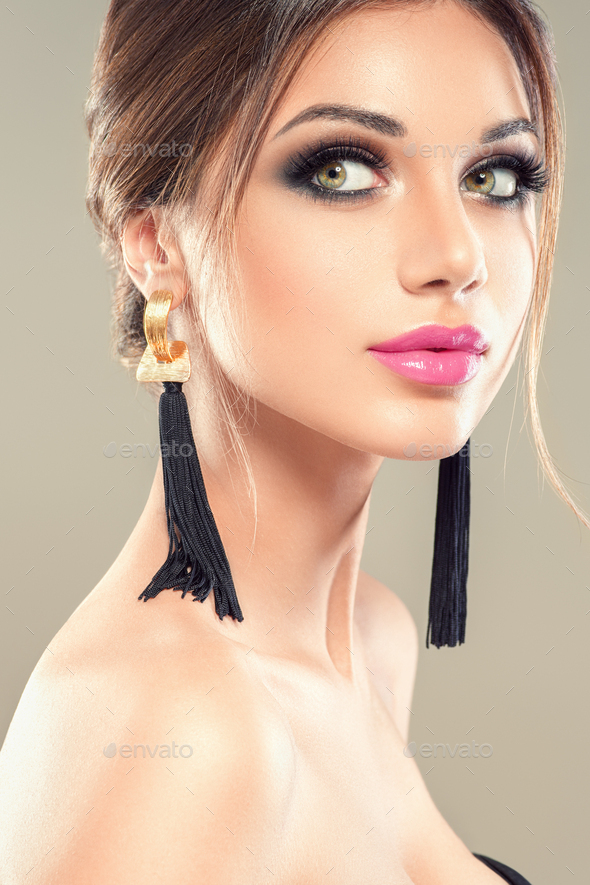 Beauty brunette woman portrait makeup earrings beautiful hairstyle beauty lips lashes eyes. On gray.