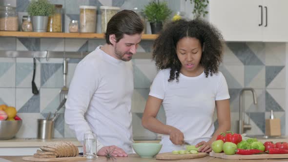 Mixed Race Couple Cutting Vegetables While Standing in Kitchen alt