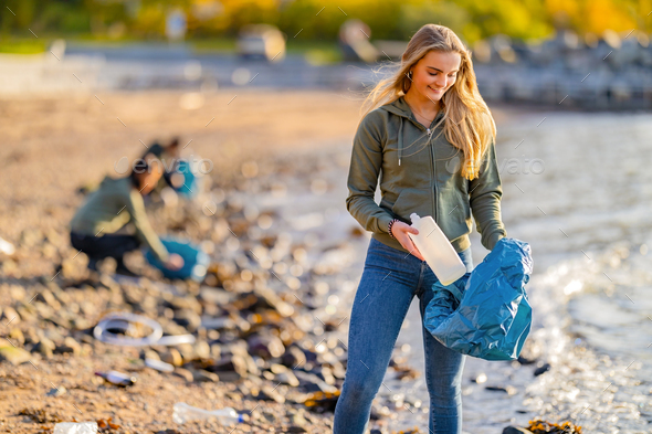 Smiling Young Female Volunteer holding bottle and garbage bag at beach - Stock Photo - Images