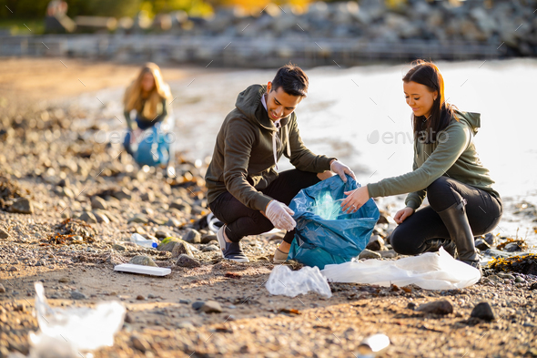 Team of dedicated and smiling volunteers collecting garbage at beach - Stock Photo - Images