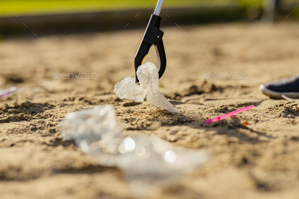 Close-up up of volunteer picking up garbage with grabber at beach - Stock Photo - Images
