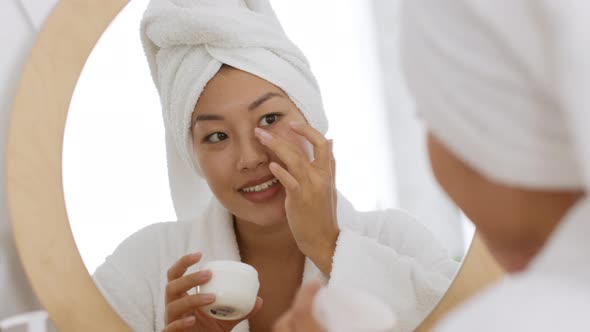 Young Carefree Korean Woman Applying Moisturizing Cream on Face Doing Beauty Care Procedures After alt